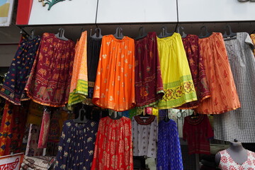 Small shop owner indian man selling shawls, clothing and souvenirs at his store. Colorful traditional Indian costume/outfit for women on mannequins. : Udaipur India - June 2020