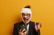 © WHstudio Leushin N - Health restrictions and medical insurance concept. Funny disabled man stares at smart phone display, gestures actively, reads funny news, has missing teeth, broken nose and shiner after street fight