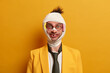 Funny positive bruised man has good sense of humor, got traumas after boxing with someone, doesnt care about injuries, wears medical bandage on hurt head, isolated on yellow studio background