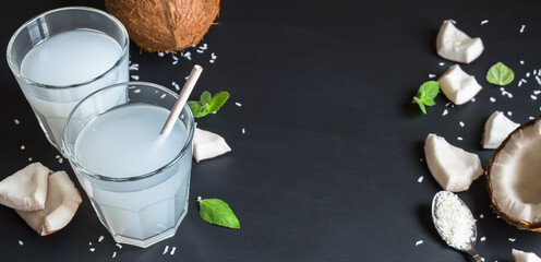 Coconut water in two glasses and ingredients on a dark background. Healthy vegetarian drink. Banner and copy space