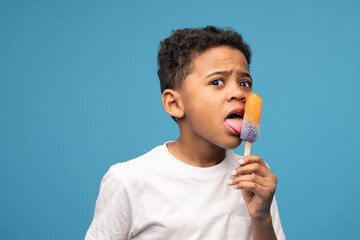 Little boy of African ethnicity licking ice cream with taste of juicy orange