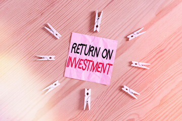 Poster - Writing note showing Return On Investment. Business concept for reviewing a financial report or investment risk analysis Colored clothespin papers empty reminder wooden floor background office