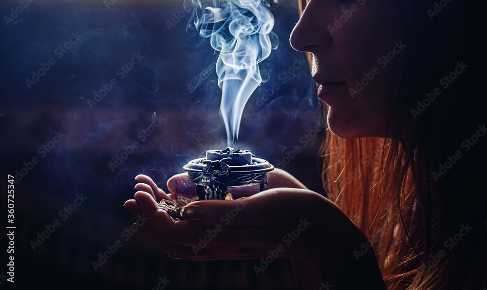 incense in a woman hand, incense smoke on a black background. - obrazy, fototapety, plakaty 