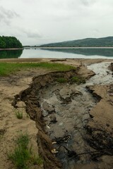 Poster - Vertical shot of cracked muddy surface by the lake surrounded by hills on a rainy day