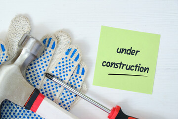 Repairman working tools with a sticker and an inscription on it under construction on a white wooden background