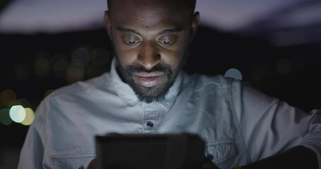 Afro american man in urban city street at night texting on tablet computer with bokeh and neon city lights in background