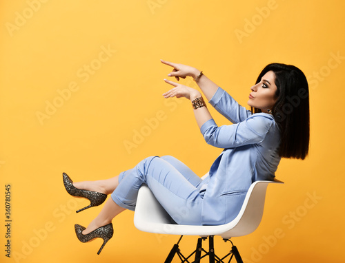 Fotomural Young woman in official suit and high-heeled shoes sitting in an armchair pointi