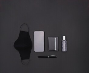 Wall Mural - Top view of a mask, smartphone, cardholder, hand sanitizer, and ballpen on a black background