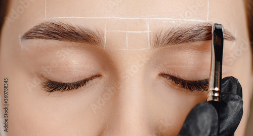 Correction and tint of eyebrows, master applies brush to woman marking on brow