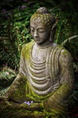 Sticker - Vertical shot of a Buddha statue with moss on top and greenery on the background