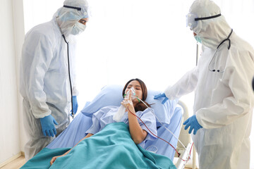 A patient woman wear face mask and cure on bed and covid-19 emergency treatment in a hospital room, doctors wear uniform protection