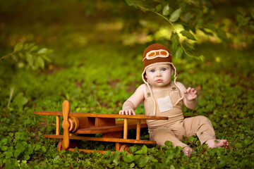 Happy little infant boy of 8-12 months old is flying on a plane in nature. Baby pilot