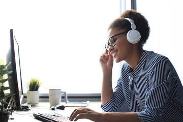 Portrait of beautiful young african american woman working on computer and chatting sitting in earphones.