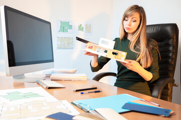 Poster - girl architect while working. architect holds a wooden model of house. a woman measures layout with 