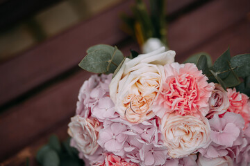 a bouquet in delicate pastel colors of pink white and lilac flowers lies on a wooden brown background on the bouquet are two two gold rings