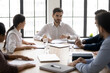 © fizkes - Confident businessman team leader holding corporate meeting in boardroom, sitting at table with diverse employees team, discussing strategy or project statistics, business partners negotiation