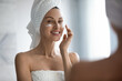 Beautiful young lady after shower look in mirror apply moisturizing facial cream or mask, smiling woman do morning daily beauty procedures in bathroom use revitalizing face lotion, skincare concept