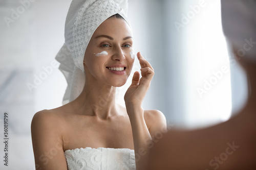 Fotografía Beautiful young lady after shower look in mirror apply moisturizing facial cream