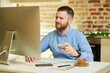 © Roman Tyukin - A man with a beard sits in front of the computer and holding a credit card at his hand at home. A guy doing an online payment on the internet on a desktop computer in his apartment.