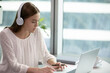 © fizkes - Girl employee in headphones enthusiastically work at a laptop and look at screen. Manager make video call and communicate with client, call center worker at workplace in office