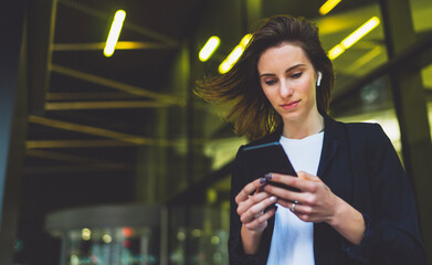 Wall Mural - concentrated businessman wearing black suit using modern smartphone near office, successful employer chats mobile phone while standing near skyscraper office on background nigh flare light