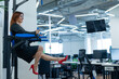 © Михаил Решетников - Happy red-haired business woman doing press exercises on a mounted horizontal bar in the office. A female employee in an official suit does sports at the workplace during the break.