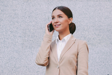 Portrait young beautiful successful business woman in suit talk mobile phone and smile on gray background. Attractive happy girl professional entrepreneur call on cell phone. Business communication