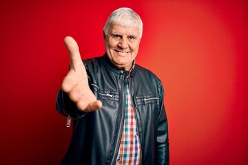 Wall Mural - Senior handsome hoary man wearing casual shirt and jacket over isolated red background smiling friendly offering handshake as greeting and welcoming. Successful business.