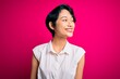 © Krakenimages.com - Young beautiful asian girl wearing casual summer shirt standing over isolated pink background looking away to side with smile on face, natural expression. Laughing confident.