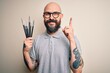 © Krakenimages.com - Handsome bald artist man with beard and tattoo painting using painter brushes surprised with an idea or question pointing finger with happy face, number one