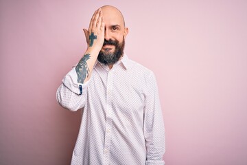 Wall Mural - Handsome bald man with beard wearing elegant shirt over isolated pink background covering one eye with hand, confident smile on face and surprise emotion.