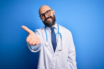 Sticker - Handsome bald doctor man with beard wearing glasses and stethoscope over blue background smiling cheerful offering palm hand giving assistance and acceptance.