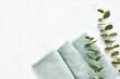 Rolled fluffy towel and green eucalyptus branch on white background. Minimalist scandinavian style. Hygiene, wellness well-being, body care concept. Copy space