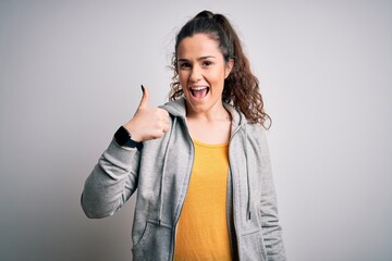 Wall Mural - Young beautiful sportswoman with curly hair wearing sportswear over white background doing happy thumbs up gesture with hand. Approving expression looking at the camera showing success.