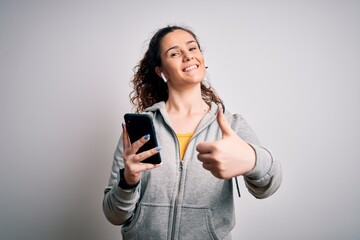 Sticker - Beautiful sportswoman with curly hair listening to music using smartphone and earphones happy with big smile doing ok sign, thumb up with fingers, excellent sign