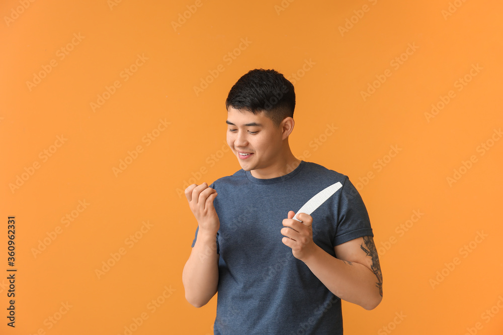 Asian man doing manicure on color background
