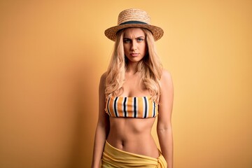 Sticker - Young beautiful blonde woman on vacation wearing bikini and hat over yellow background skeptic and nervous, frowning upset because of problem. Negative person.