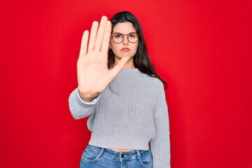 Canvas Print - Young beautiful brunette woman wearing casual sweater over red background doing stop sing with palm of the hand. Warning expression with negative and serious gesture on the face.