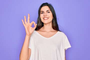 Canvas Print - Young beautiful brunette woman wearing casual white t-shirt over purple background smiling positive doing ok sign with hand and fingers. Successful expression.