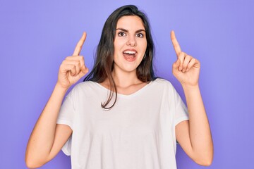 Sticker - Young beautiful brunette woman wearing casual white t-shirt over purple background smiling amazed and surprised and pointing up with fingers and raised arms.