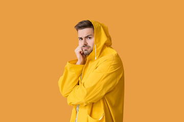 Wall Mural - Displeased young man in raincoat on color background