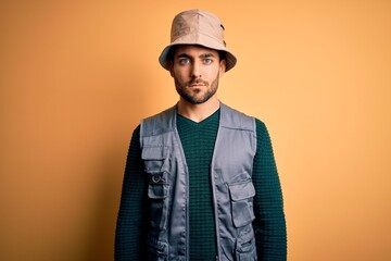 Canvas Print - Handsome tourist man with beard on vacation wearing explorer hat over yellow background Relaxed with serious expression on face. Simple and natural looking at the camera.