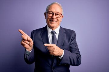 Wall Mural - Grey haired senior business man wearing glasses and elegant suit and tie over purple background smiling and looking at the camera pointing with two hands and fingers to the side.