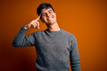 Poster - Young handsome man wearing casual sweater standing over isolated orange background Smiling pointing to head with one finger, great idea or thought, good memory