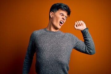 Poster - Young handsome man wearing casual sweater standing over isolated orange background stretching back, tired and relaxed, sleepy and yawning for early morning