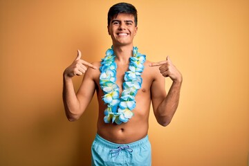 Poster - Young handsome tourist man on vacation wearing swimwear and hawaiian lei flowers looking confident with smile on face, pointing oneself with fingers proud and happy.