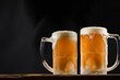 two cold mugs with beer, with overflowing foam, on wooden table and dark background, space for writing