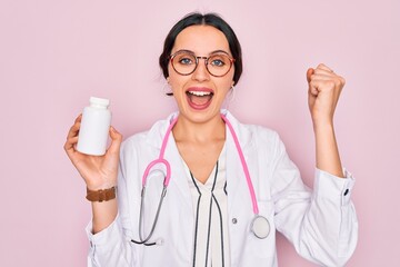 Wall Mural - Young beautiful doctor woman with blue eyes wearing stethoscope holding medicine pills screaming proud and celebrating victory and success very excited, cheering emotion