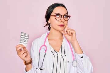 Wall Mural - Young beautiful doctor woman with blue eyes wearing stethoscope holding medicine pills serious face thinking about question, very confused idea