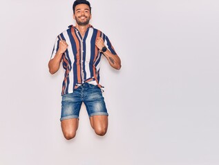 Young handsome hispanic man wearing casual clothes smiling happy. Jumping with smile on face celebrating with fists up over isolated white background